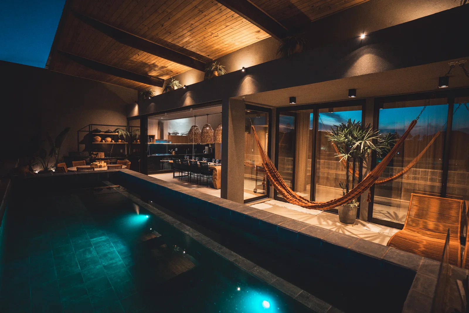 A piscina privativa ao anoitecer, com as redes e a área gourmet iluminada ao fundo.