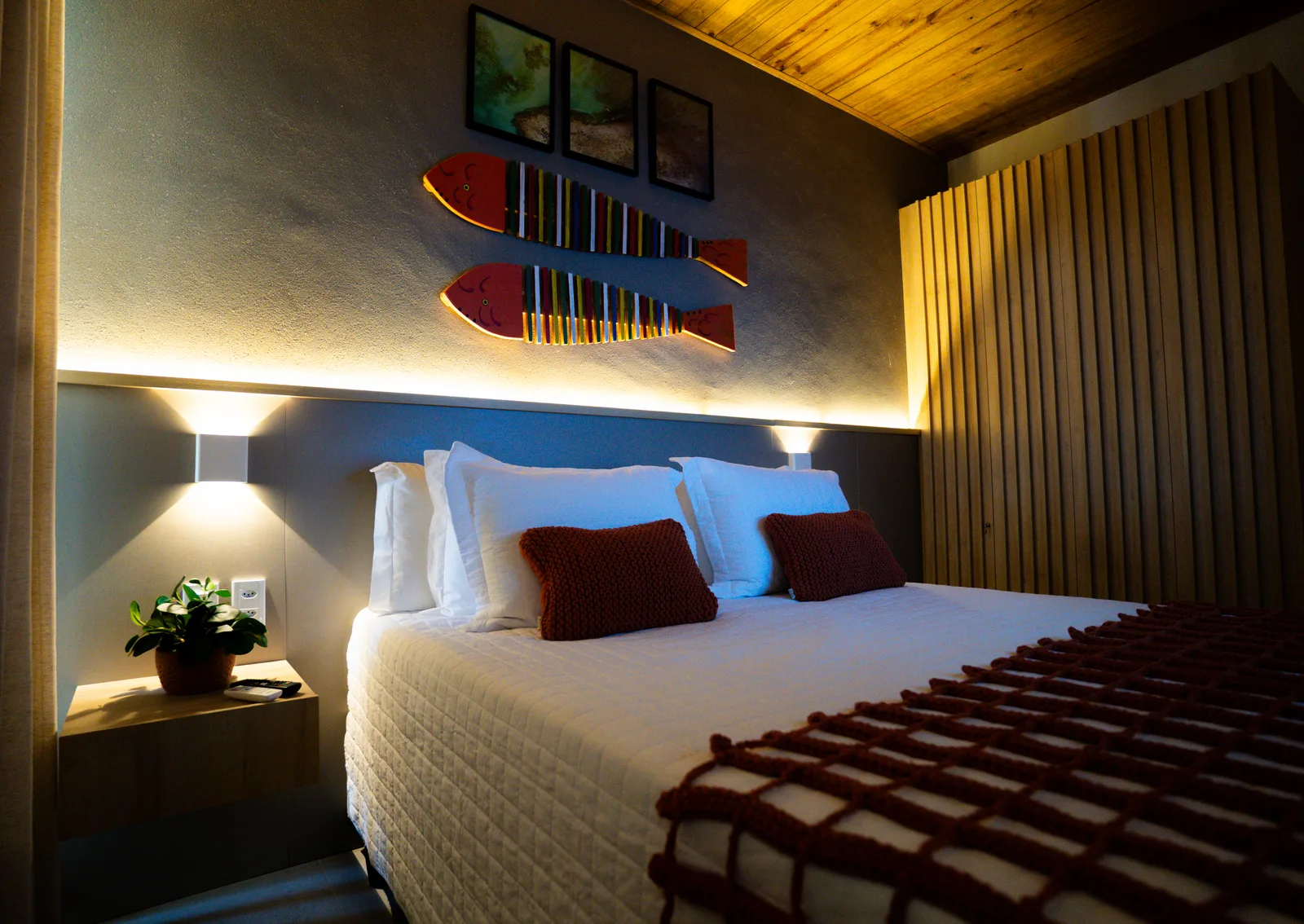 Suíte com cama box Queen, cabeceira ripada e luminárias de leitura.